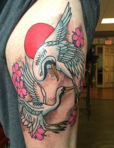 Jesse Britten Tattoo, St. Augustine, FL Japanese tattoo of two white cranes with pink cherry blossoms and a red sun on a person's thigh.