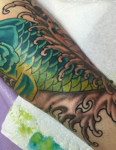 Jesse Britten Tattoo, St. Augustine, FL Japanese tattoo of a blue and green koi fish swimming in stylized waves on a forearm.
