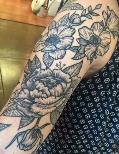 Floral tattoo art on arm featuring detailed peony and other flower designs in black ink. Jesse Britten Tattoo, St Augustine FL, Black and Grey tattoo
