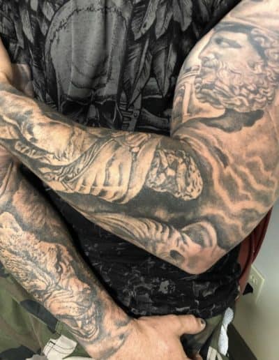 Jesse Britten Tattoo, St. Augustine, FL - Man's arms with detailed black and gray tattoos of a lion and a classical figure.