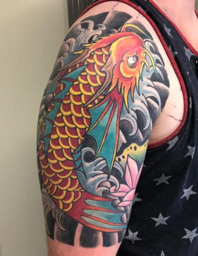 Jesse Britten Tattoo, St. Augustine, FL Japanese tattoo of a vibrant koi fish with red, yellow, and blue scales surrounded by swirling waves and a lotus flower.