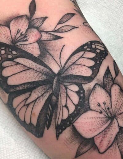 Jesse Britten Tattoo, St. Augustine, FL Butterfly tattoo with floral accents on arm. Black and white ink design.