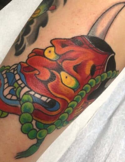 Jesse Britten Tattoo, St. Augustine, FL Red oni mask Japanese tattoo with green beads and a single horn.