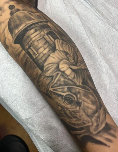 Jesse Britten Tattoo, St. Augustine, FL Black and gray tattoo of a frog, sentry box, and castle turret on an arm