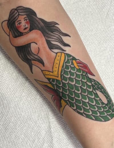 Jesse Britten Tattoo, St. Augustine, FL Traditional tattoo of a mermaid with green scales and flowing dark hair.