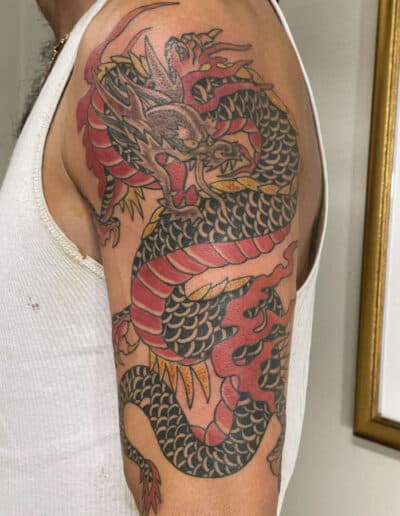 Jesse Britten Tattoo, St. Augustine, FL Dragon tattoo on arm, traditional Japanese style with red and black scales.