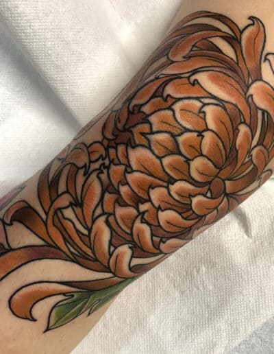 Jesse Britten Tattoo, St. Augustine, FL Orange chrysanthemum tattoo on arm, detailed floral design.