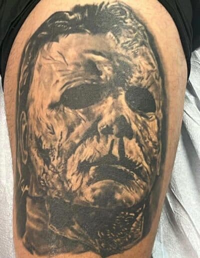 Black and gray portrait tattoo of a man's face with intense expression.