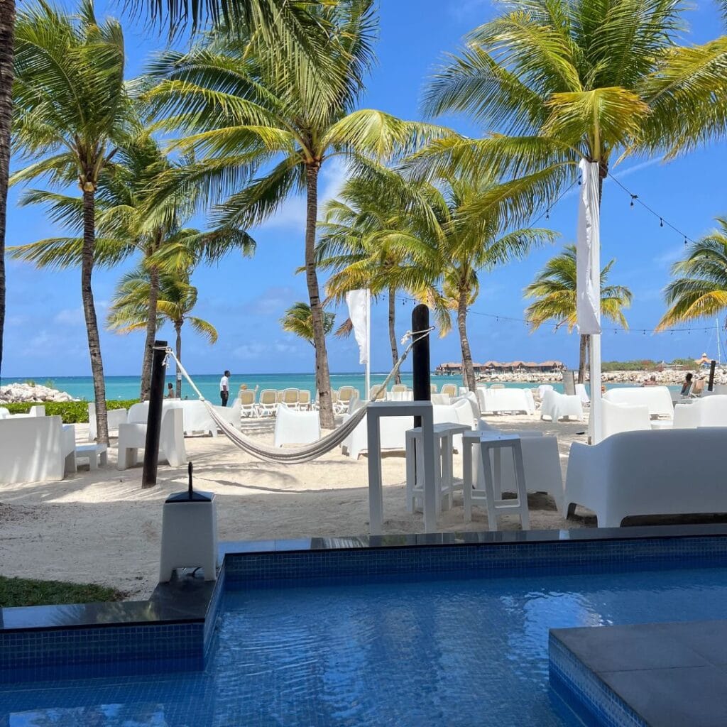 Relaxing beachside pool with palm trees, white loungers, and ocean view at luxury resort, perfect for tropical getaway, travel, and leisure with Jet Setting with Jen.