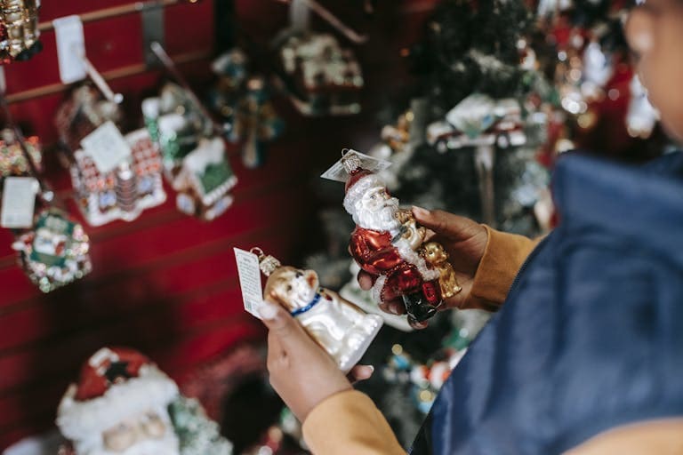 Side view of crop ethnic girl with Santa and dog toys standing in shop with Christmas decorations