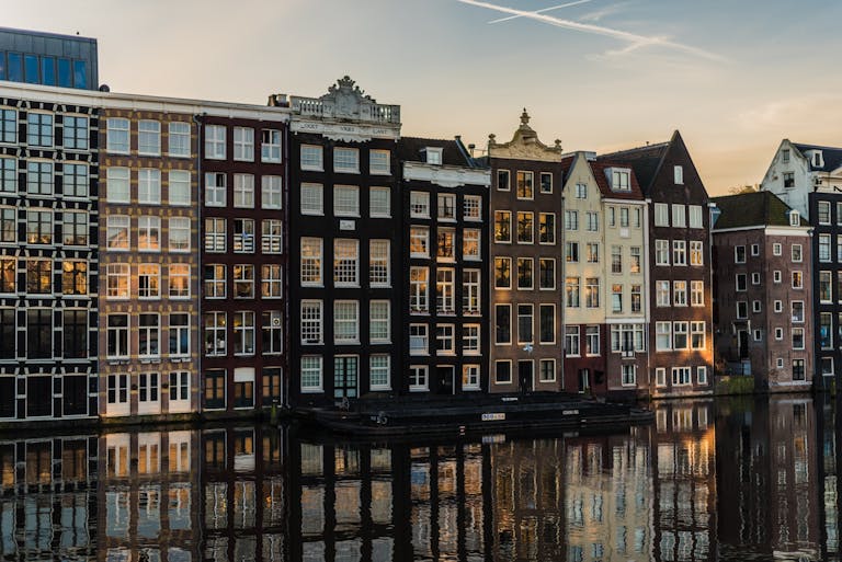Colorful historic canal houses in Amsterdam during sunset, reflecting on the water, showcasing European travel and architecture.