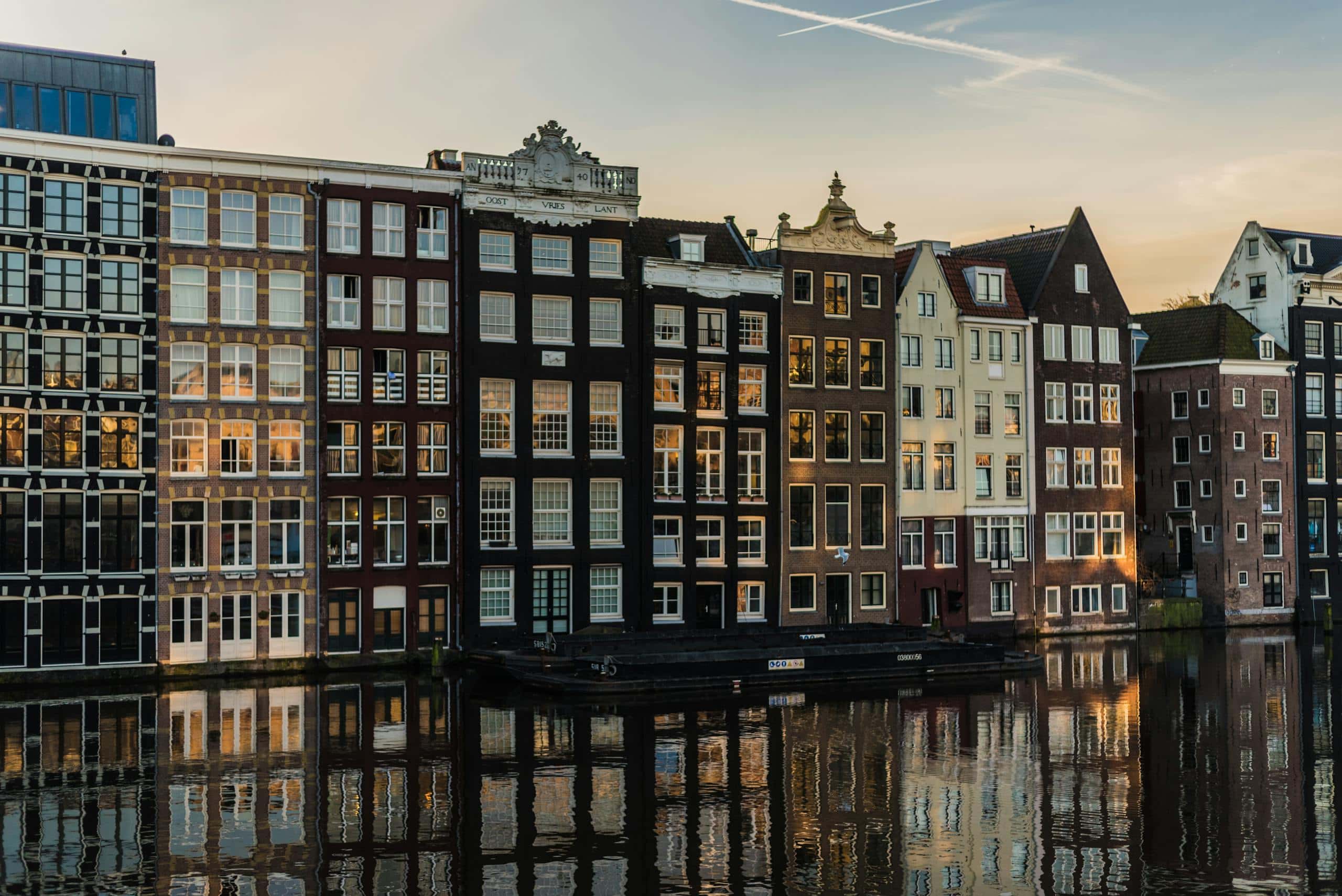 Colorful historic canal houses in Amsterdam during sunset, reflecting on the water, showcasing European travel and architecture.