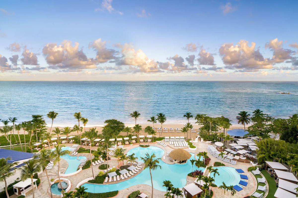 A luxurious resort in Puerto Rico with multiple pools, palm trees, and a stunning ocean view during sunset, perfect for solo female travelers.
