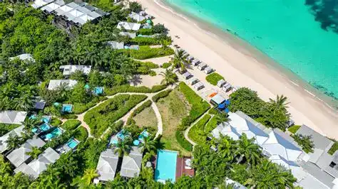 Aerial view of a luxurious Antigua beachfront resort featuring lush gardens, private villas, and a pristine sandy beach with turquoise waters, perfect for a relaxing tropical getaway.