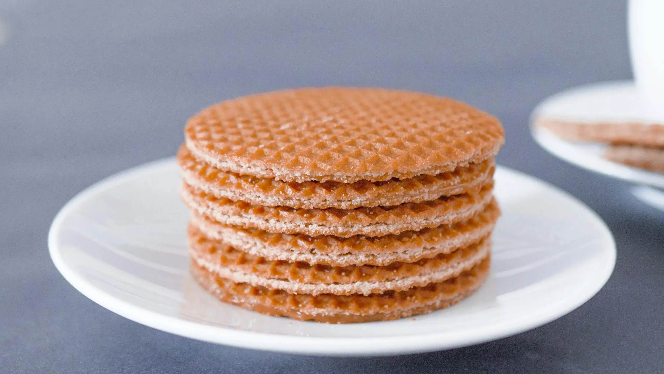 Golden caramel waffle cookies stacked on a white plate, close-up.