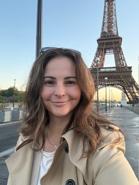 Eiffel Tower with a smiling solo female traveler in Paris during daytime, capturing the essence of visiting Paris as a solo female traveler in any season.