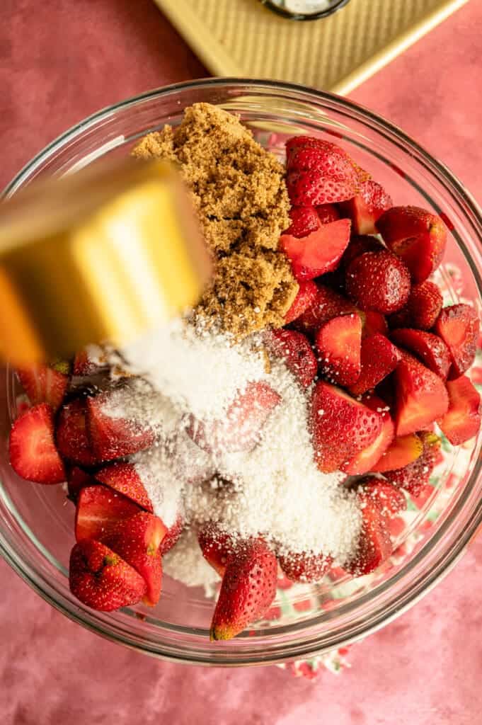 pouring sugar into a bowl of ingredients for a strawberry pie recipe