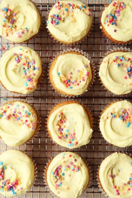 A dozen vanilla cupcakes on a wire rack