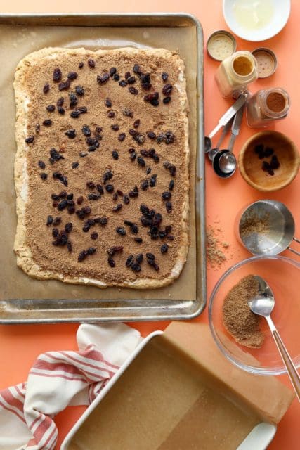 Gluten free carrot cake cinnamon roll dough pressed out and sprinkled with sugar and raisins.