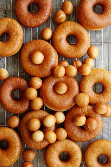 Fried doughnuts and doughnut holes cooling on a wire rack.