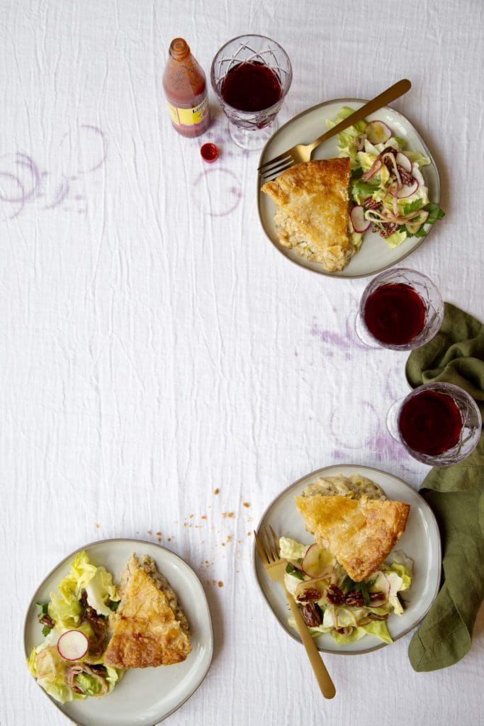 Slices of Crawfish Pie on plates with green salad and glasses of wine.