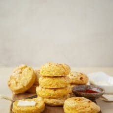 Sweet potato biscuit recipe stacked on a cutting board with butter.