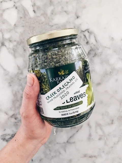 Hand holding jar of greek oregano.