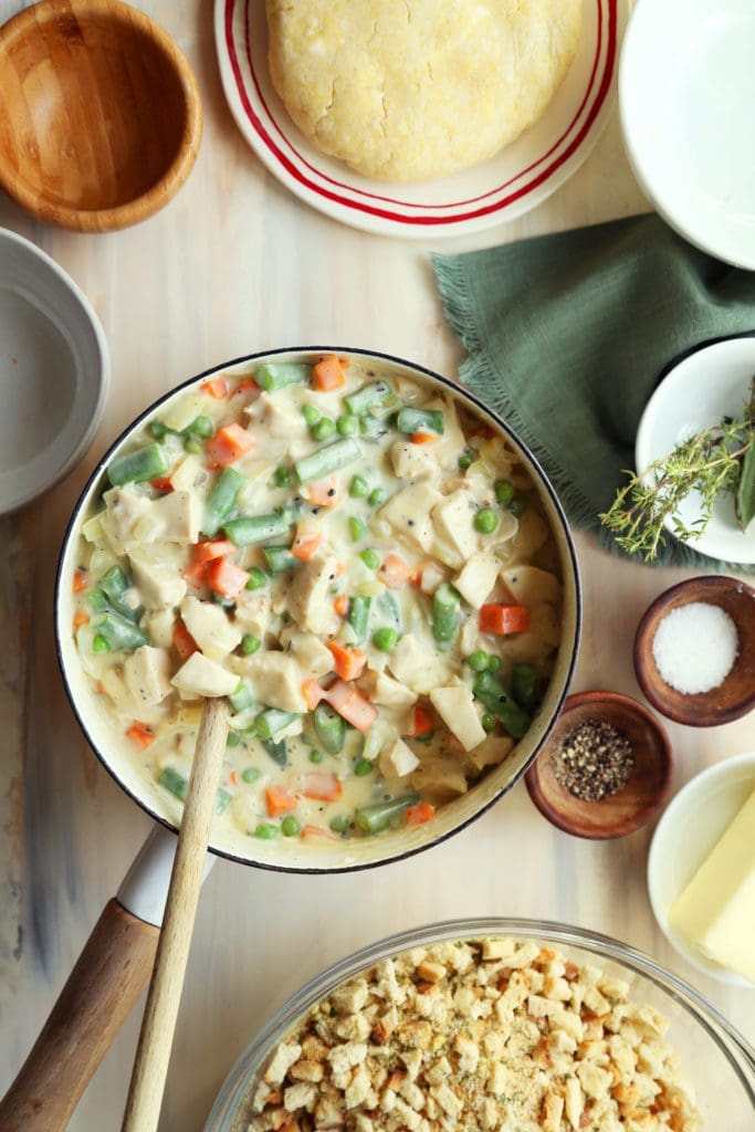 Adding cream sauce to turkey and vegetables in a large pot for turkey pot pie s