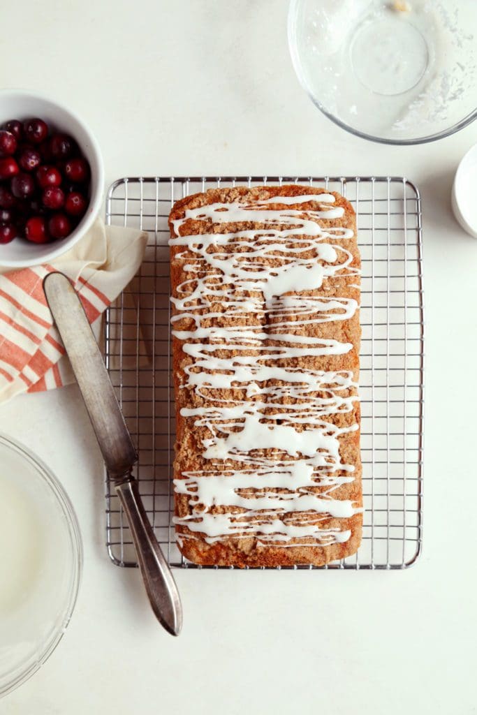 Baked loaf of cranberry orange bread on cooling rack with glaze.