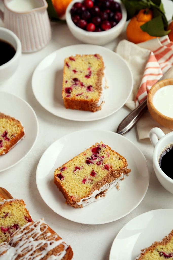 Slices of cranberry orange bread on white plates with coffee.