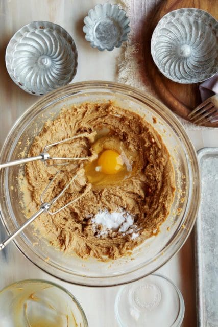 Eggs and baking soda added to peanut butter cookie recipe in a clear bowl with beaters.