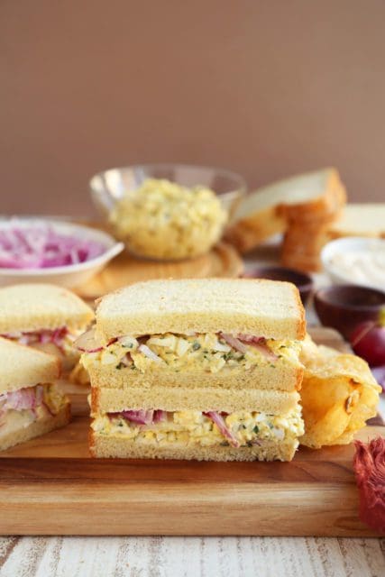 Two egg salad sandwiches on a cutting board with chips.