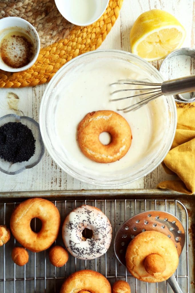 Fried doughnut getting dipped in lemon glaze.
