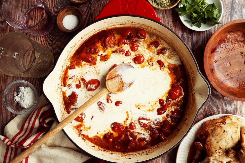 Cream added to marry me chicken recipe in skillet with tomatoes.