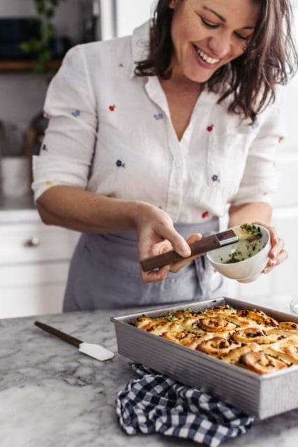 Joy using a pastry brush to spread garlic butter on baked rolls.