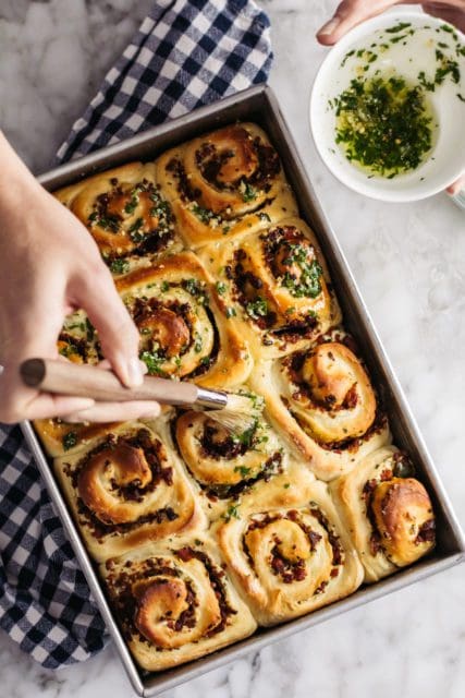 Brushing garlic butter on baked sausage rolls.