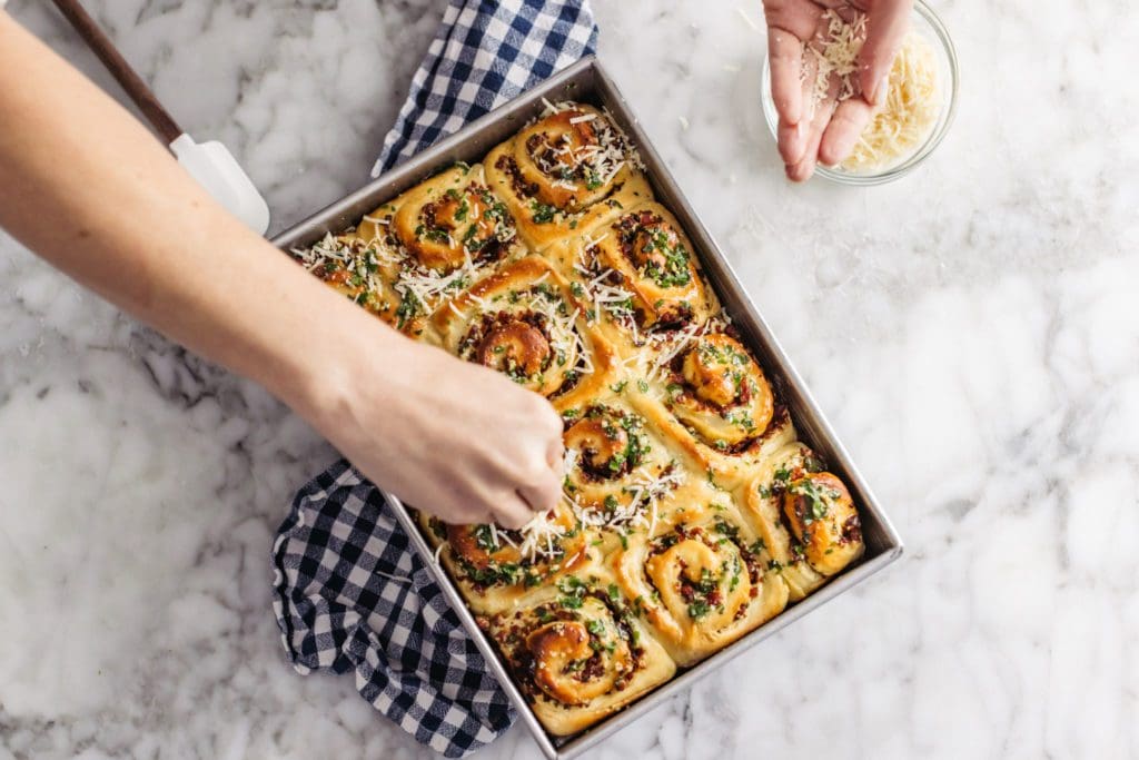 Sprinkling parmesan cheese on baked rolls.