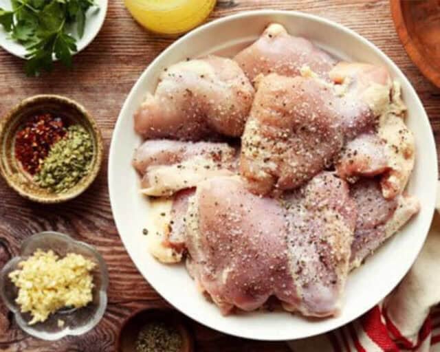 Chicken thighs seasoned in a bowl.