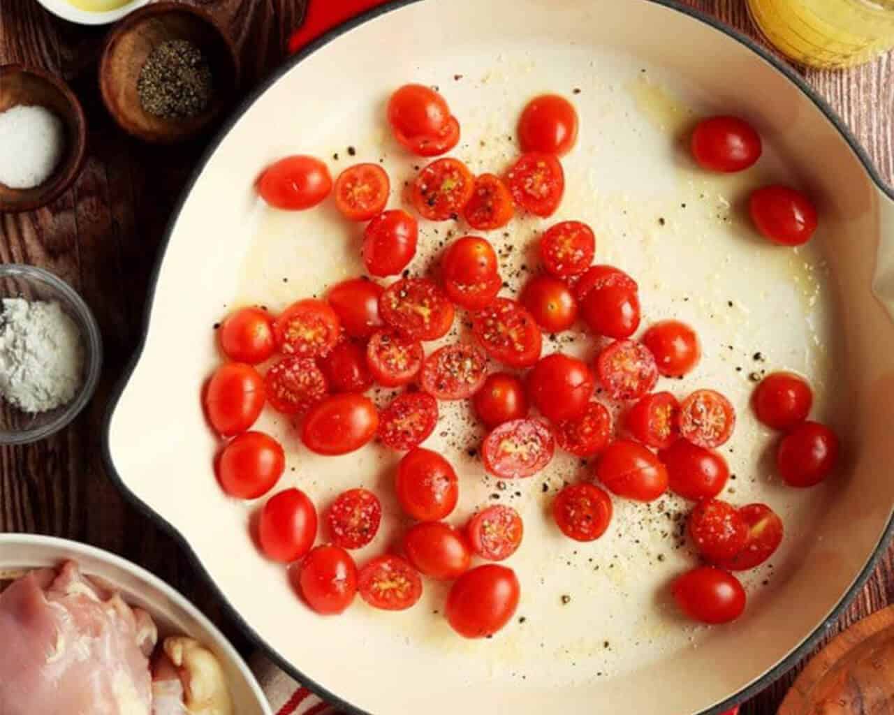 Cherry tomatoes halved in a skillet with salt and pepper for roasting.