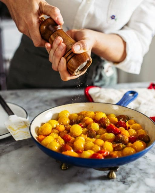 Adding black pepper to cooked cherry tomatoes in pan.