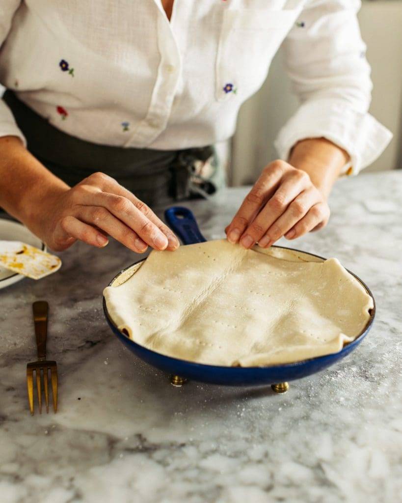 Placing puff pastry on top of cherry tomatoes in cast iron pan.
