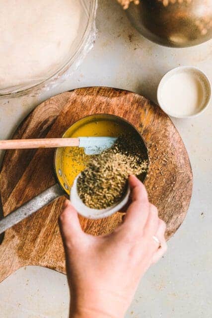 Pouring herbs into a pot of melted butter for pull apart garlic bread.