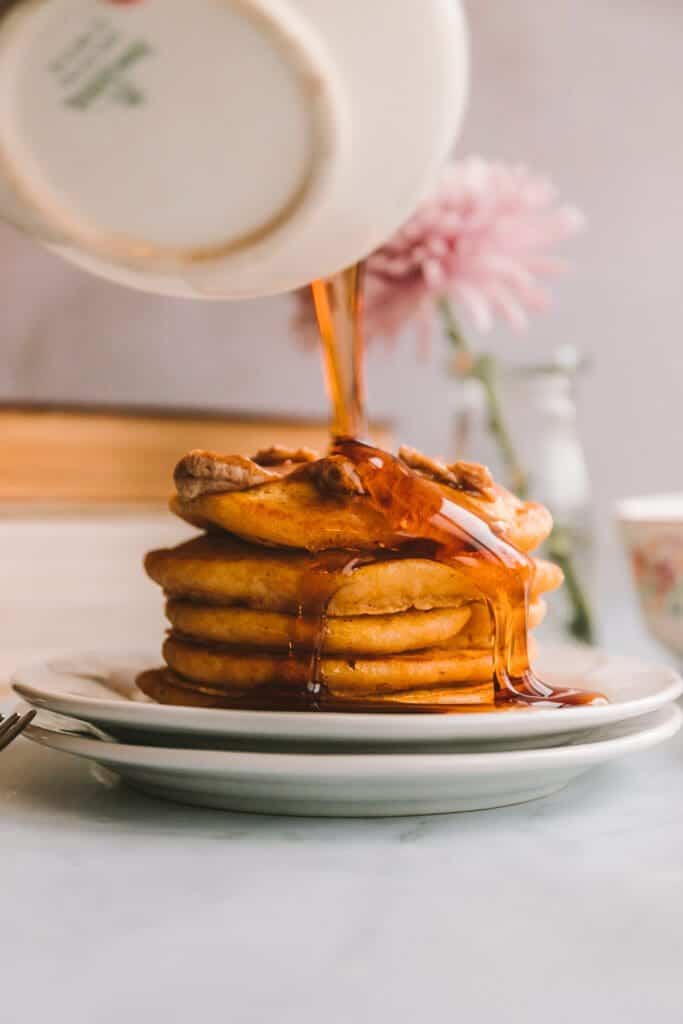 pouring maple syrup over stack of pancakes.