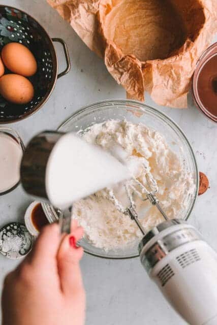 Pouring sugar into cream cheese for chocolate basque cheesecake recipe