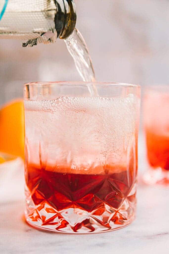Pouring prosecco into a glass to make a negroni sbagliato