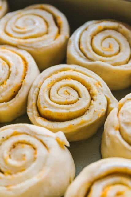 Puffy orange rolls risen in pan.
