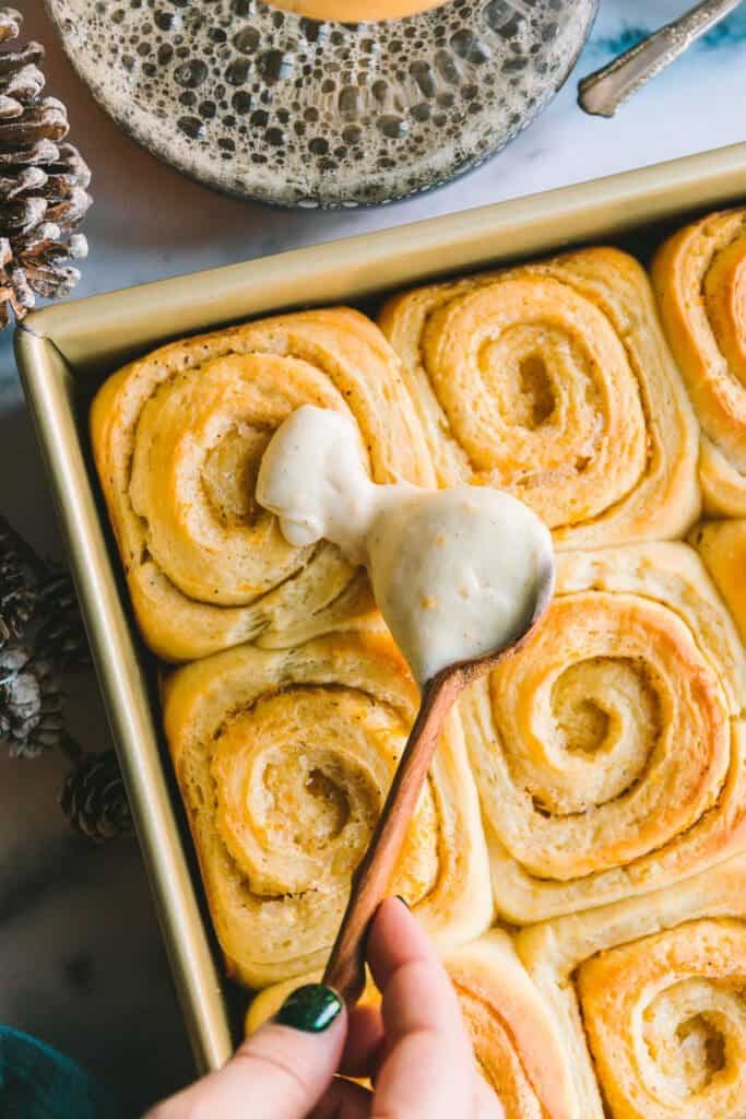 Spreading cream cheese glaze onto rolls.