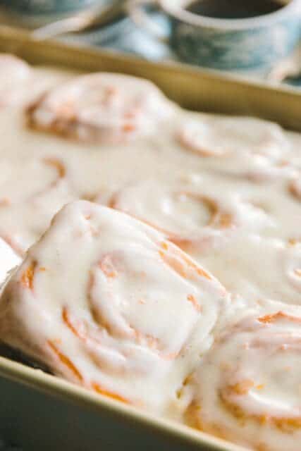 Scooping glazed orange rolls from the pan