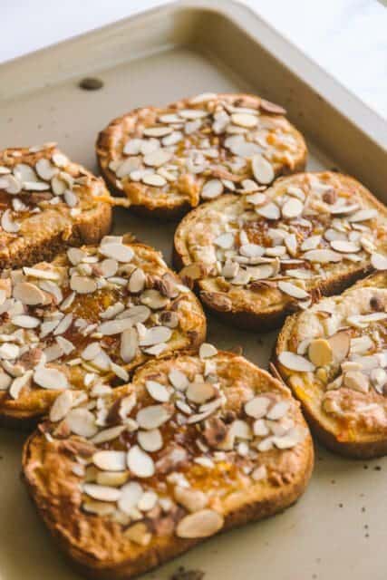 Mardi Gras king cake toast on a baking sheet with sliced almonds
