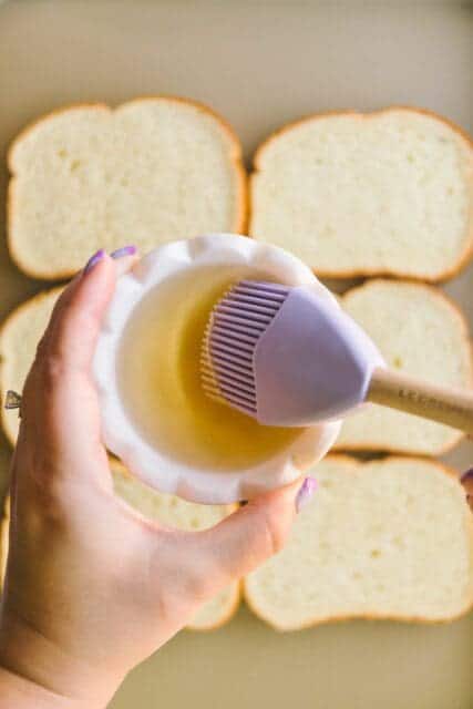 brushing simple syrup on toast lined on a baking pan for bostock pastry.